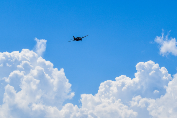 Image of a plan flying in the sky amongst white fluffy clouds.