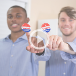 Image of two young men holding up "I Voted Today!" stickers. A play button shows that clicking the image will play a video.