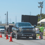 Image of vehicles waiting in line on the road at a Sheriff's checkpoint.