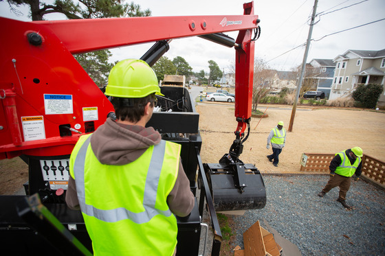 Image of a man operating heavy machinery to lift and deposit items in a large trash container.