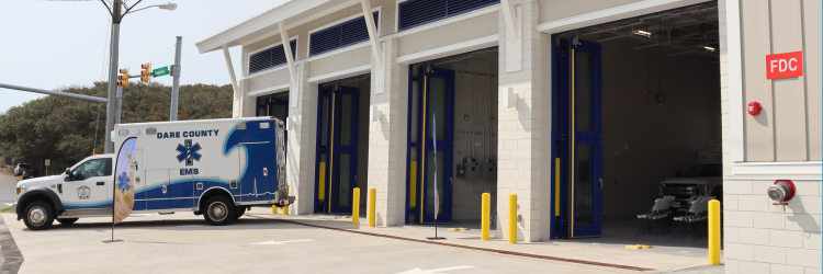 Image of the EMS Station 4 exterior with all four bay doors open and an ambulance parked in front of the western-most bay door.