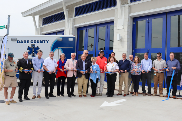 Image of a large group of people standing together ceremoniously cutting a ribbon in front of the new EMS Station 4 facility.