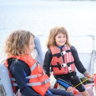 Image of two kids sitting on a boat wearing life preservers.