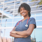 Image of a nurse standing in front of a building smiling with her arms crossed confidently.