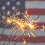 Image of an American flag with sparklers in the foreground. 