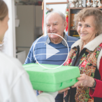 Image of a woman handing an elderly couple a covered dish. A play button sits over the image signifying "click to watch the video."