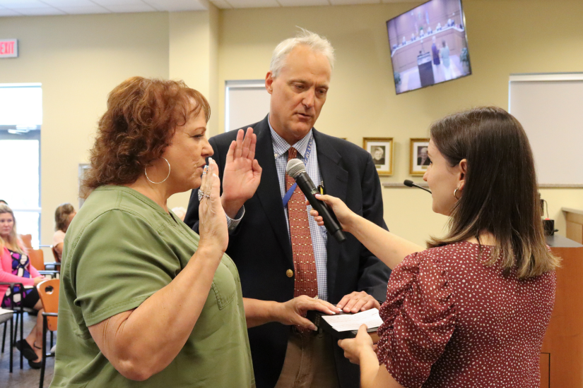 Image of Clerk to the Board  Skyler Foley swearing in Hosea Wilson and Becky Huff, whose hands rest on a Bible.