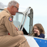 Image of a man in uniform assisting children tour an antique airplane.