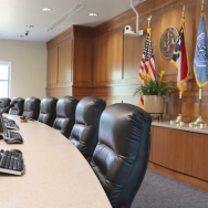 Image of empty Board of Commissioners chairs around a curved dais with the U.S., N.C. and Dare County flags in the back of the room. 