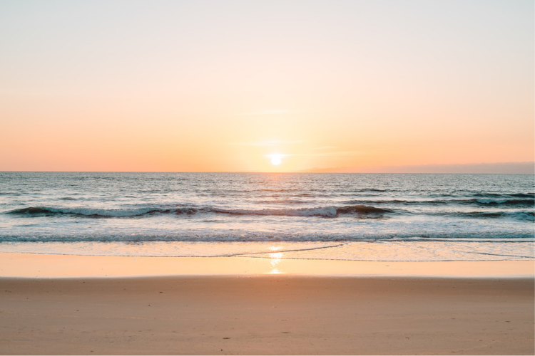 Image of the sun rising over a peaceful beach in Dare County.