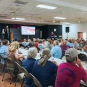 Image of a large seated group of older adults listening to a speaker at the Baum Senior Center.