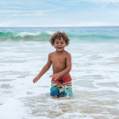 Image of a young boy smiling as he wades out of the ocean.