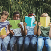 Image of four children sitting outdoors reading.
