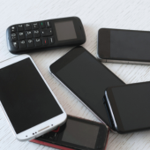 Six old cell phones lay on a tabletop.
