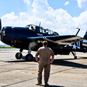 Image of a man in a flight mechanic uniform standing in front of a blue Air Force commemorative plane.