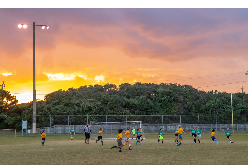 Image of the sun setting as children play a game of Parks & Recreation soccer. 