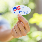 Image of a woman holding up a sticker that reads, "I Voted".