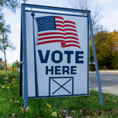 Image of a sign by the street that reads, "Vote here"