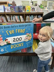 Child holding "I've read 200 books" sign for 1000 books before kindergarten program