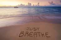 Calm water at the beach with "Just Breathe" written in the sand