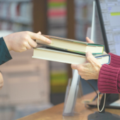 A librarian hands books to a patron at a library.