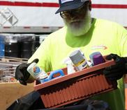 Image of a man with a beard wearing gloves properly disposing of old cans of spray paint.