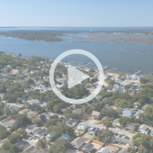 Aerial photo of houses along the water on Colington Island. Play button shows that a video about Outer Banks stories will play when clicked.