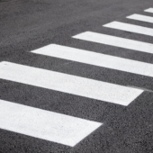 Image of white lines over pavement, signaling a crosswalk in a roadway.