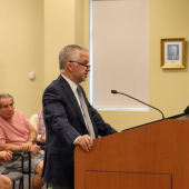 Image of a man in a suit speaking at a podium.