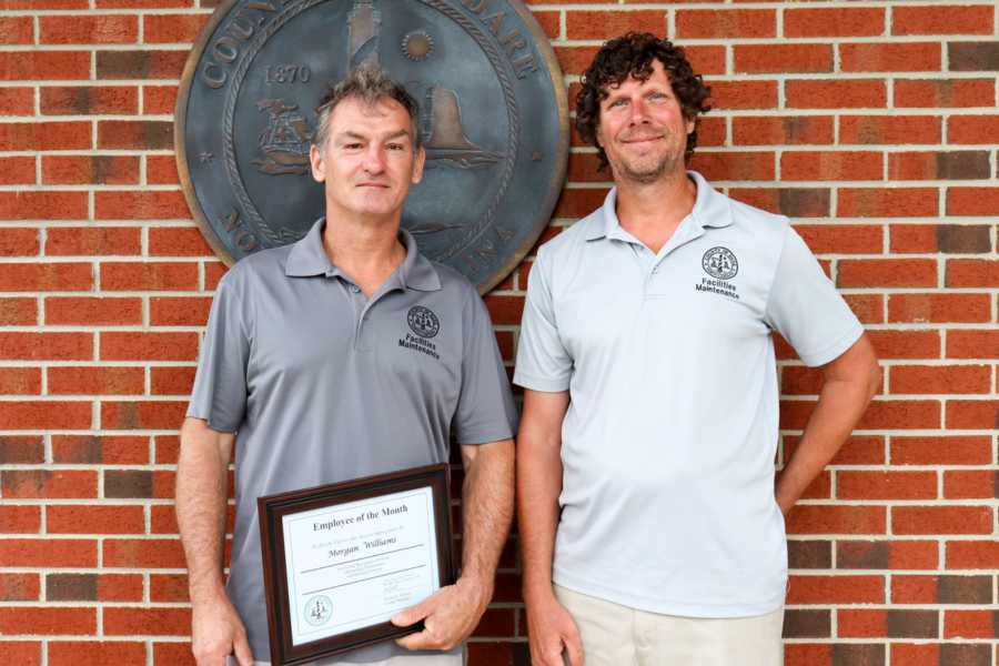 Morgan Williams and Gordon Price stand together in front of the bronze Dare County seal.
