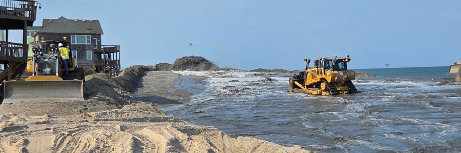 Image of beach nourishment underway along the beaches of Buxton. Heavy equipment pushes sand.