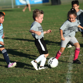 Four young children kick a soccer ball together during a Dare County Parks & Recreation game.