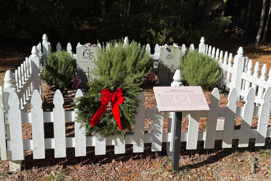 Image of a wreath placed on a small cemetery with a white picket fence around it.