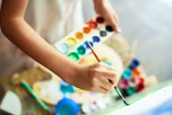 A person holds a palate of colorful paints and uses a brush to paint on a canvas.