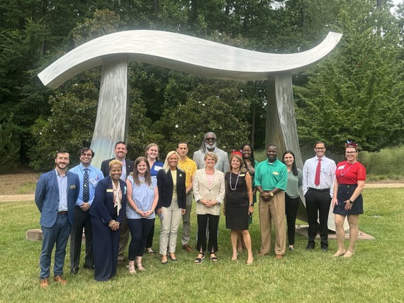 A group of people standing in front of a sculpture of the pie symbol outside 