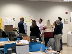 a group of people standing and looking at chart paper on a wall and having a discussion 
