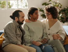 Teen sitting at home on sofa in between male adult and female adult
