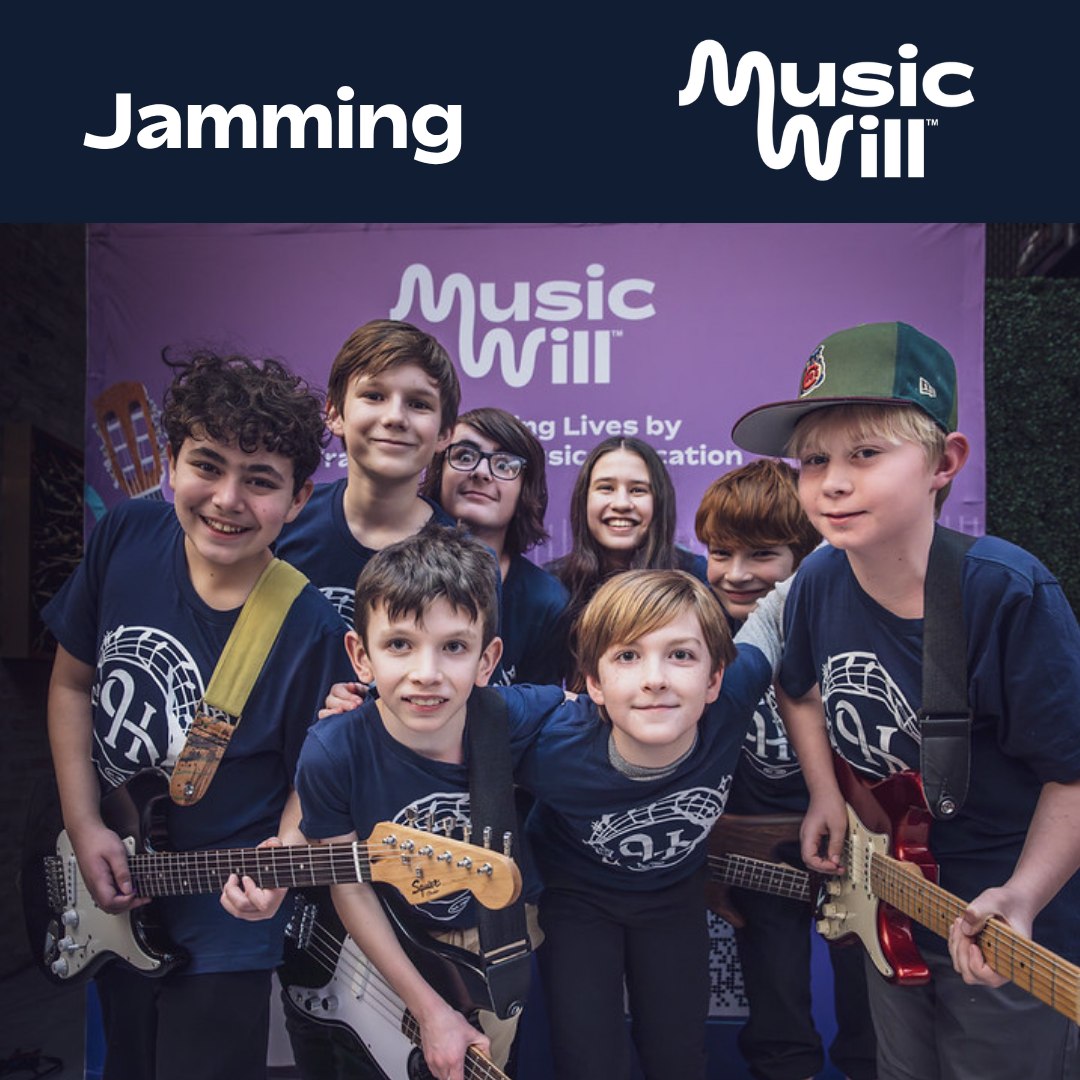 A group of seven happy young students posing together holding electric guitars in front of a purple "Music Will" backdrop.