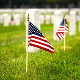 Graveyard with headstone in the background and small American flags in foreground.
