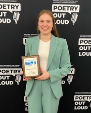 2025 ND State Poetry Out Loud Champion Leah Hochhalter standing in front of a POL banner, holding her ND state plaque