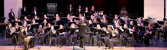 Bismarck's St. Mary’s Central High School Wind Orchestra students in all black, sitting on stage with their instruments