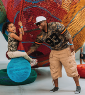A man wearing army clothing, smiling and laughing with his daughter as she plays at a museum