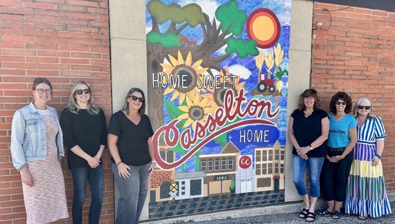 six people standing on either side of a mural saying Home Sweet Casselton Home