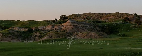 Photo by Jill Edinger of North Dakota badlands during the summer, showing green grass and blue sky