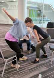Taryn Johnson (light blue sweatshirt), Joan Meggitt (presenter), and John (seated) creating a movement in the Dance for Parkinson’s seminar.