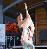 teaching artist Lexy Liu performing a traditional Chinese dance in full attire with a red dragon behind her