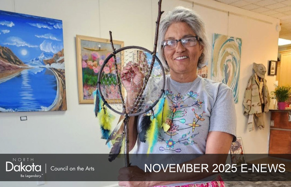A smiling Ojibwe artist, Roxanne Laducer, holds up a large dreamcatcher she created in her studio.