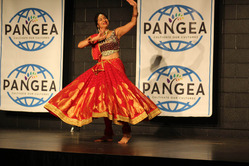 A joyful woman in traditional red and gold Indian attire dances on a stage with "Pangea" banners.