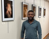 Ekow Ephrim  standing next to an exhibit of his photographs in the ND Gov Staff Offices hallway