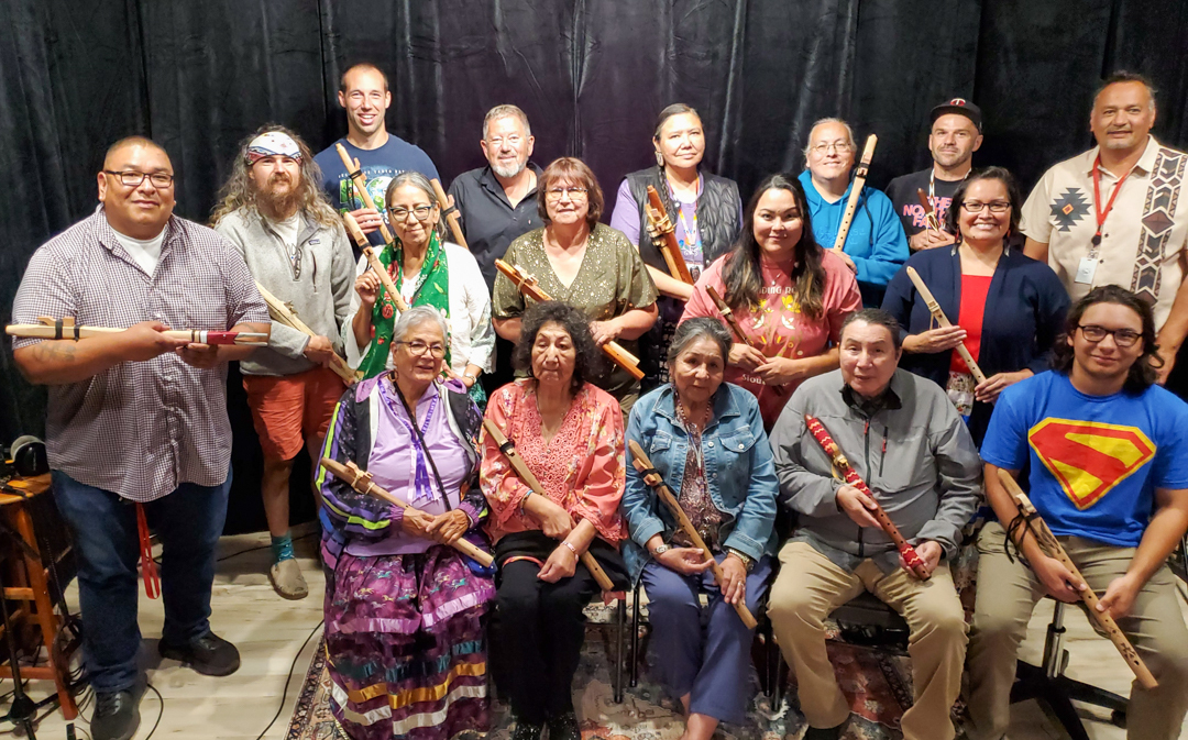 A group of people sitting and standing together. They are all holding wooden flutes.